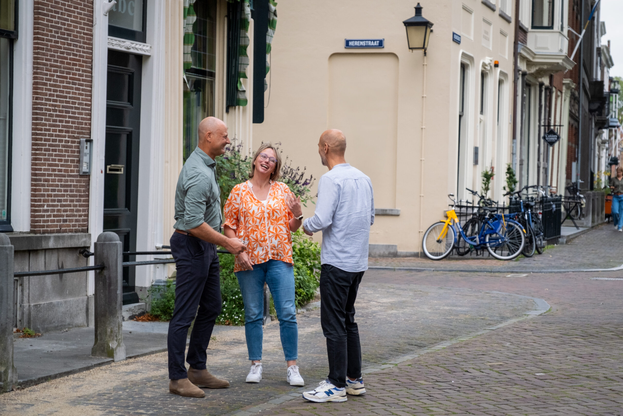 Drie mensen staan op een bakstenen stoep.