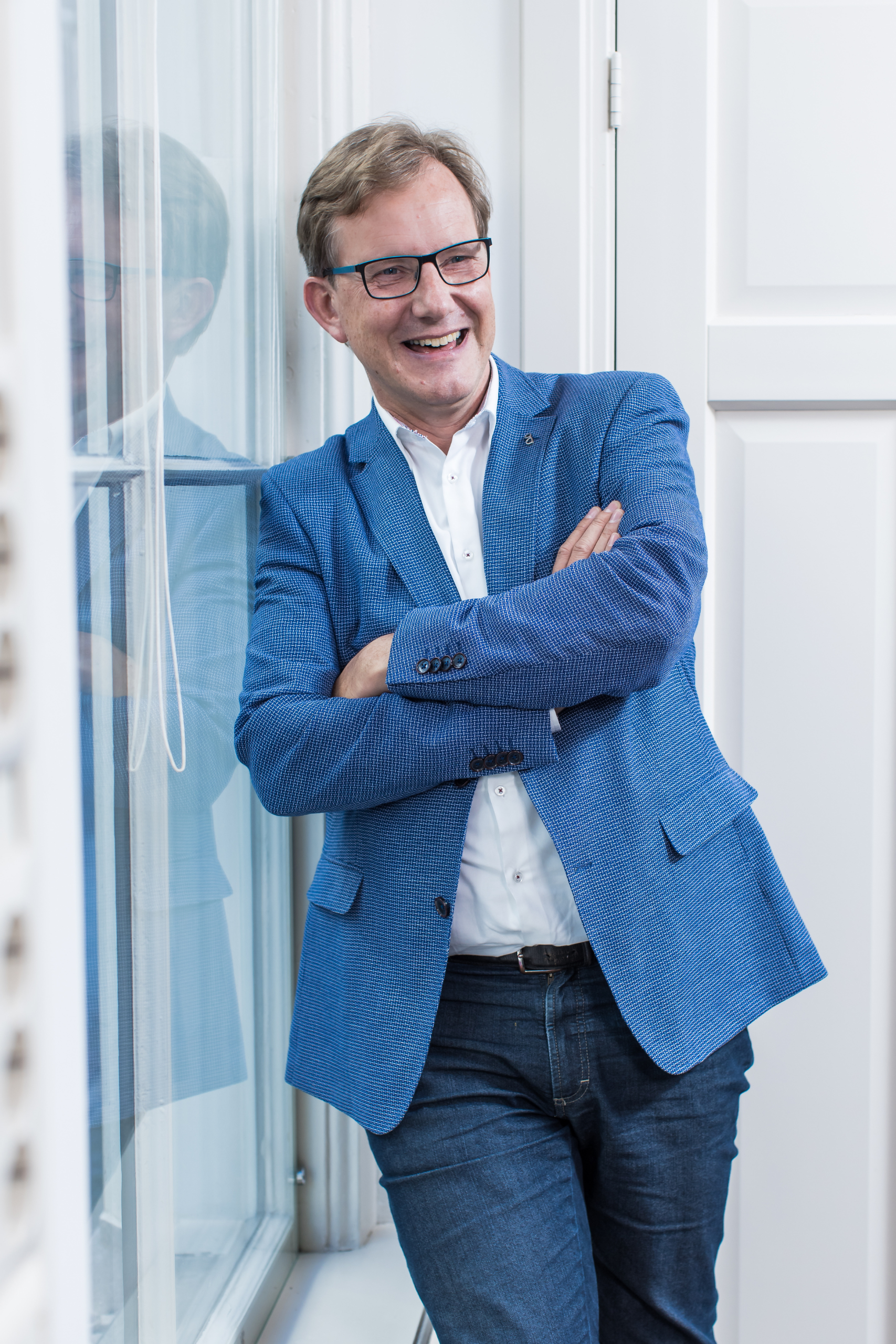 Een man in een blauw jasje leunend tegen een raam.