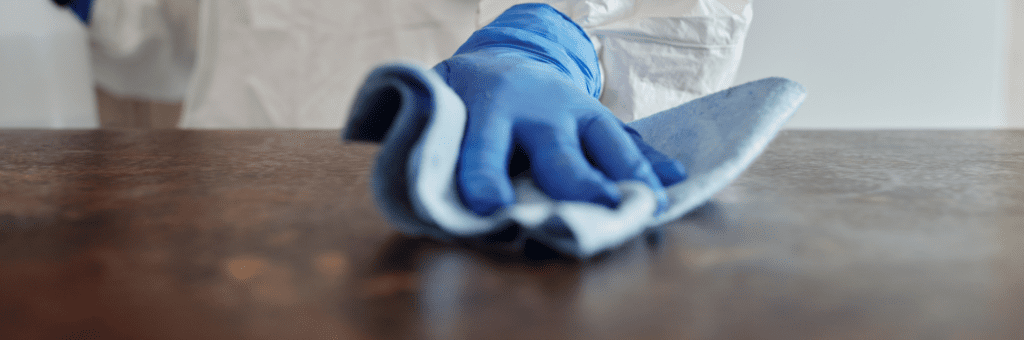 Een persoon die blauwe handschoenen draagt, veegt een doek af op een tafel.