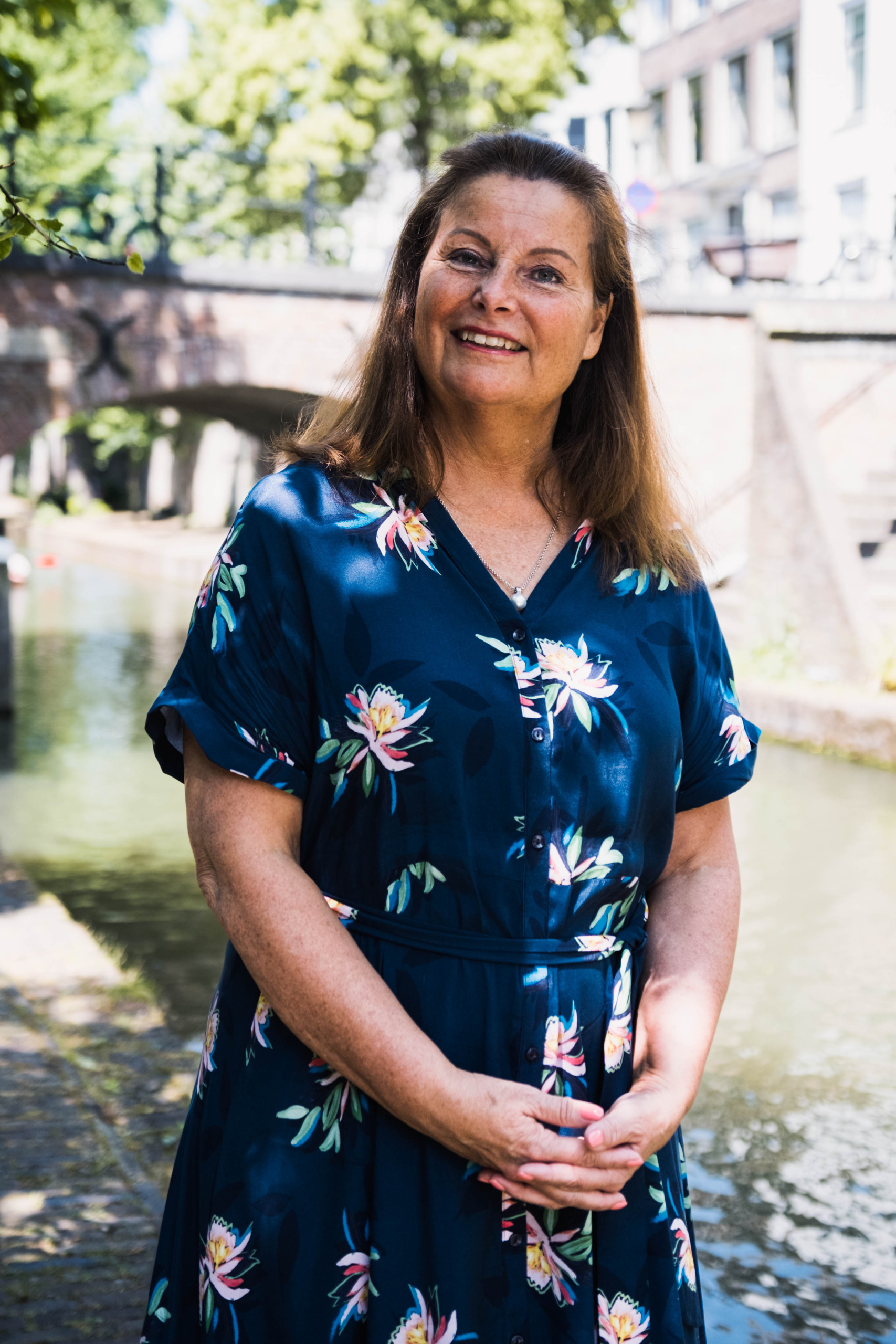 Een vrouw in een gebloemde jurk staande voor een gracht.
