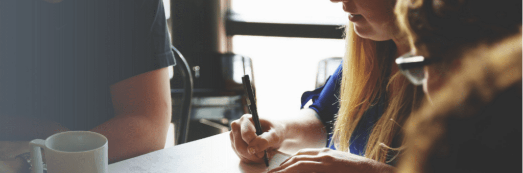 Een groep mensen zit aan een tafel en schrijft op een stuk papier.