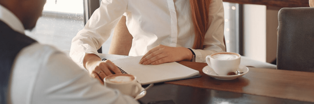 Een vrouw zit aan een tafel en schrijft in een notitieboekje.