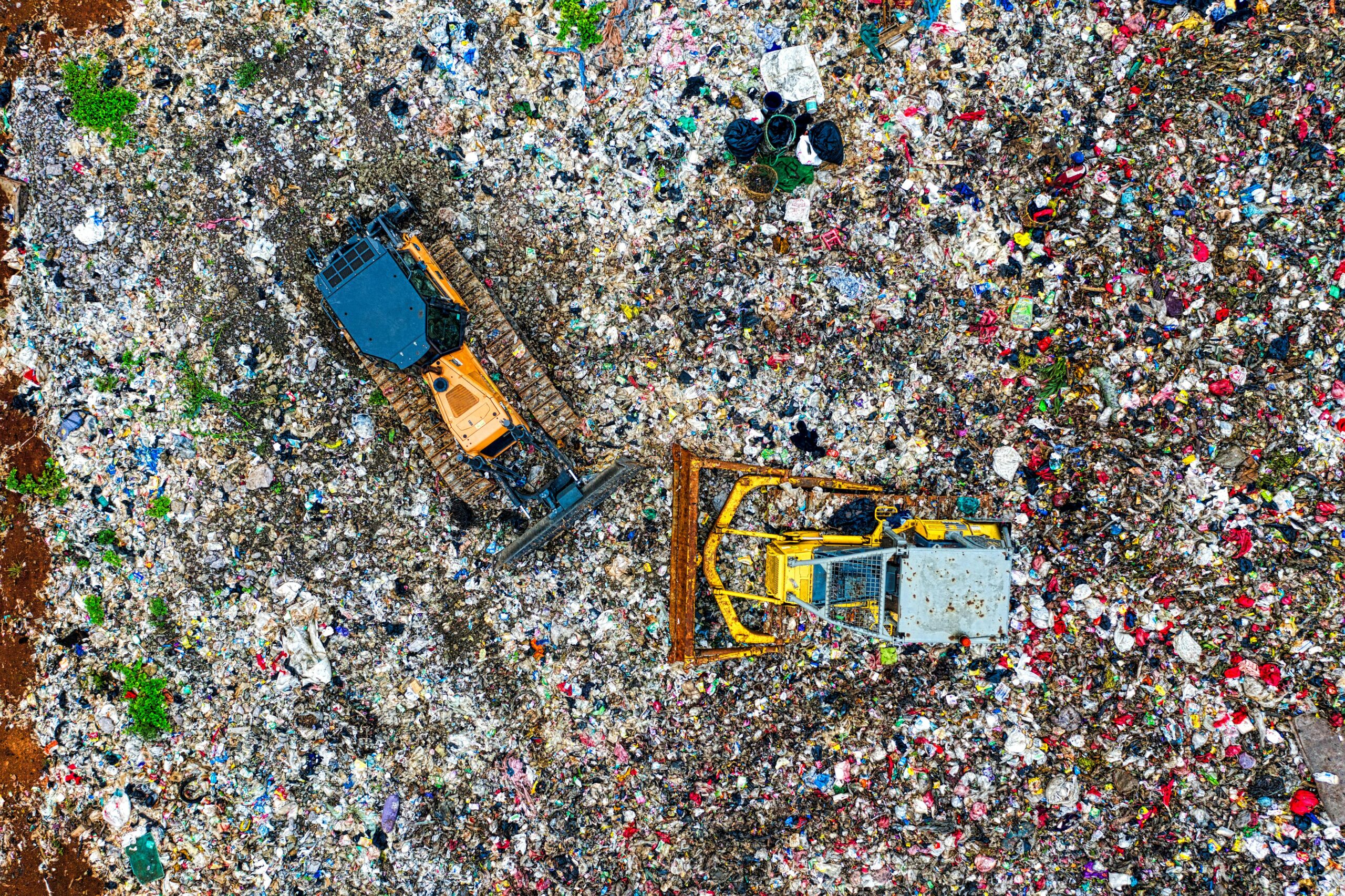 Luchtfoto van twee bulldozers die door een grote stortplaats werken, gevuld met allerlei soorten afval en puin.