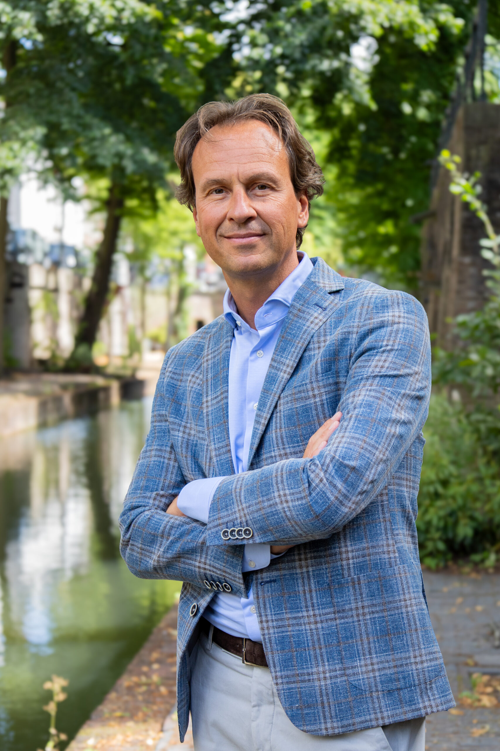 Paul van der Heijden, directeur VFM. Een man in een blauw geruite blazer staat buiten met gekruiste armen, glimlachend, bij een kanaal en groen.